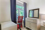 This bright and airy room features a comfortable red office chair positioned by a large window, offering a pleasant view of lush greenery.