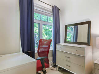 This bright and airy room features a comfortable red office chair positioned by a large window, offering a pleasant view of lush greenery.
