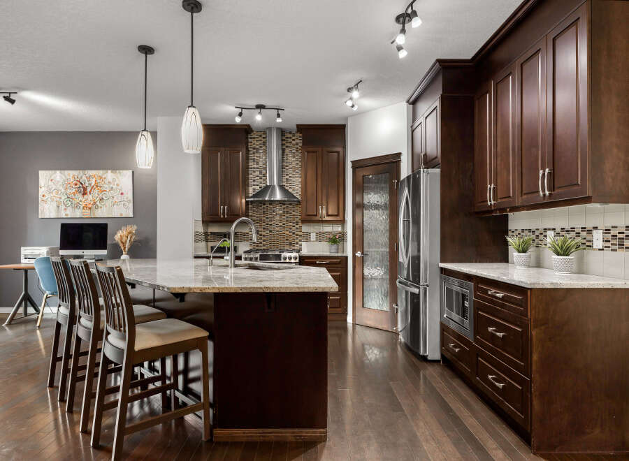 Experience luxury in this stunning kitchen featuring dark wood cabinetry, a granite island with bar seating, and a sleek stainless steel range hood.