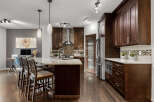 Experience luxury in this stunning kitchen featuring dark wood cabinetry, a granite island with bar seating, and a sleek stainless steel range hood.