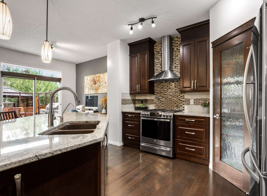 Experience luxury in this stunning kitchen featuring dark wood cabinetry, granite countertops, and a sleek stainless steel range with a mosaic tile backsplash.