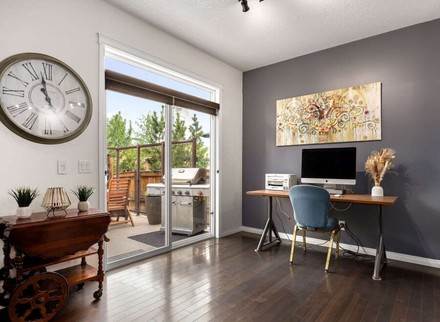 This inviting home office space features a large wall clock and a sliding glass door that opens to a patio with a grill.