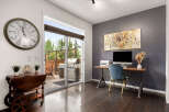 This inviting home office space features a large wall clock and a sliding glass door that opens to a patio with a grill.