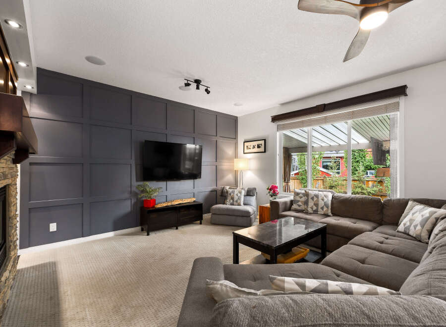 Experience modern living in this spacious living room, featuring a striking dark gray accent wall with a geometric design that perfectly complements the large flat-screen TV.