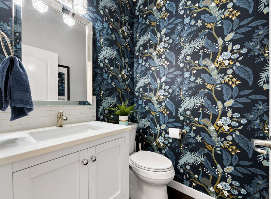 This stylish powder room features a striking navy blue wallpaper adorned with a beautiful peacock and floral motif, adding a touch of exotic elegance.