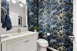 This stylish powder room features a striking navy blue wallpaper adorned with a beautiful peacock and floral motif, adding a touch of exotic elegance.