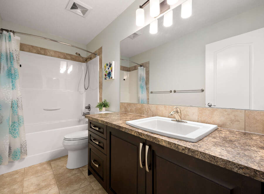 This bright and clean bathroom features a spacious white bathtub with a decorative shower curtain and a modern vanity with a white sink and ample counter space.