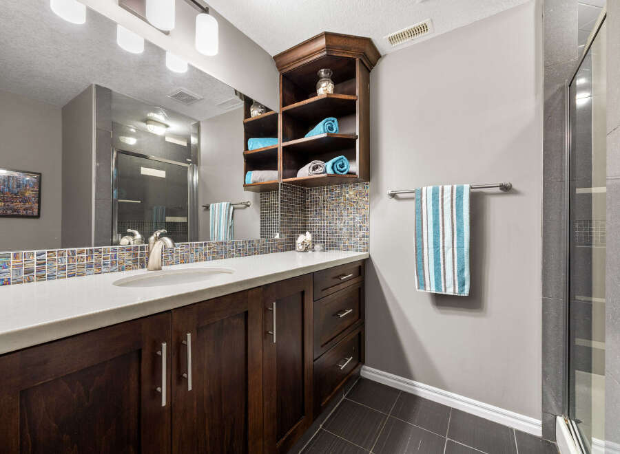 This modern bathroom features a sleek vanity with dark wood cabinetry and a white countertop, complemented by a mosaic tile backsplash.