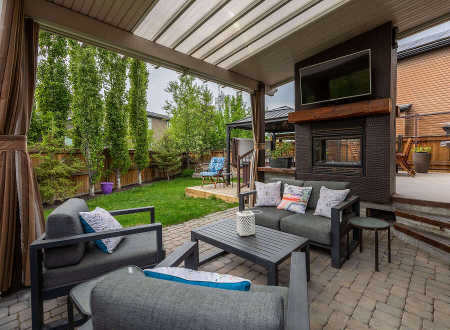 Enjoy outdoor living in this covered patio featuring a cozy seating area with a fireplace and a mounted TV.