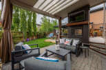 Enjoy outdoor living in this covered patio featuring a cozy seating area with a fireplace and a mounted TV.