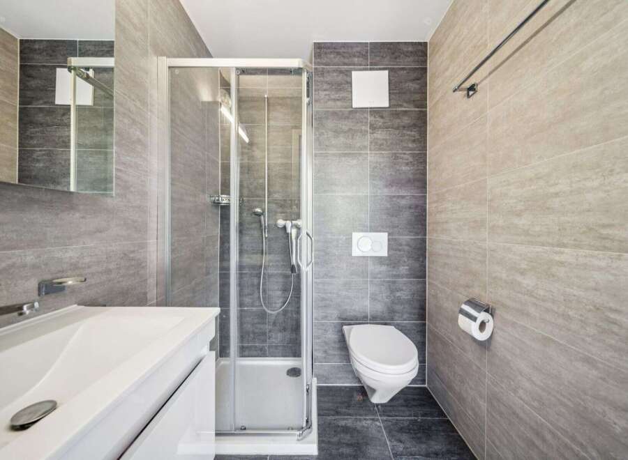 This modern bathroom features a sleek white vanity with a vessel sink, complemented by a glass-enclosed shower and a wall-mounted toilet.