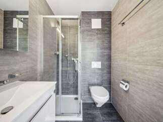 This modern bathroom features a sleek white vanity with a vessel sink, complemented by a glass-enclosed shower and a wall-mounted toilet.