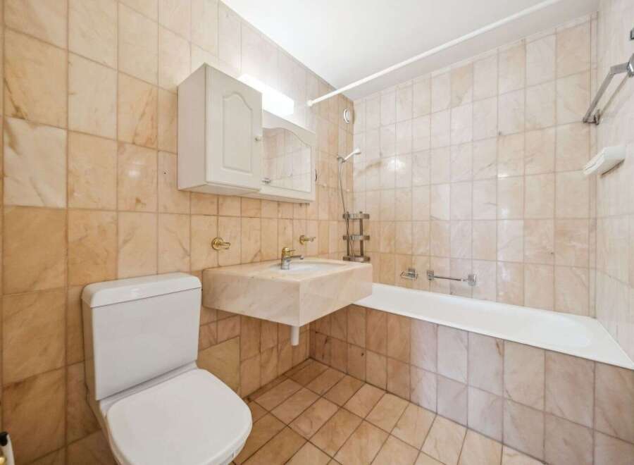 This bathroom features a classic design with beige marble tiles adorning the walls and floor, creating a warm and inviting atmosphere.