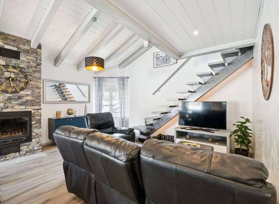 Experience modern living in this stunning living room featuring a striking stone fireplace and a sleek, floating staircase.