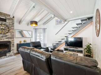 Experience modern living in this stunning living room featuring a striking stone fireplace and a sleek, floating staircase.