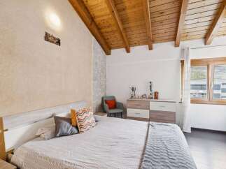 This charming bedroom features a cozy bed with patterned pillows and a soft throw, complemented by a rustic stone accent wall and a warm wooden ceiling.