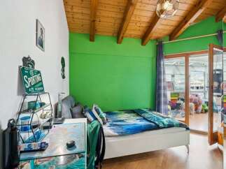 This vibrant bedroom features a comfortable white bed with a striking blue and green comforter, set against a lively green accent wall.