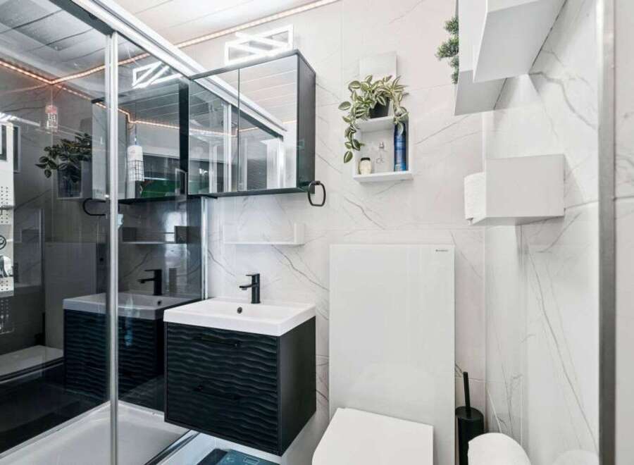 Experience modern luxury in this meticulously designed bathroom, featuring a sleek vanity with a wave-patterned facade and a stylish black faucet.