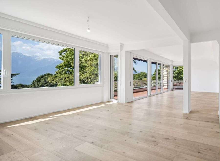 Experience breathtaking panoramic views from this spacious living area, featuring expansive windows that showcase stunning mountain and lake vistas.