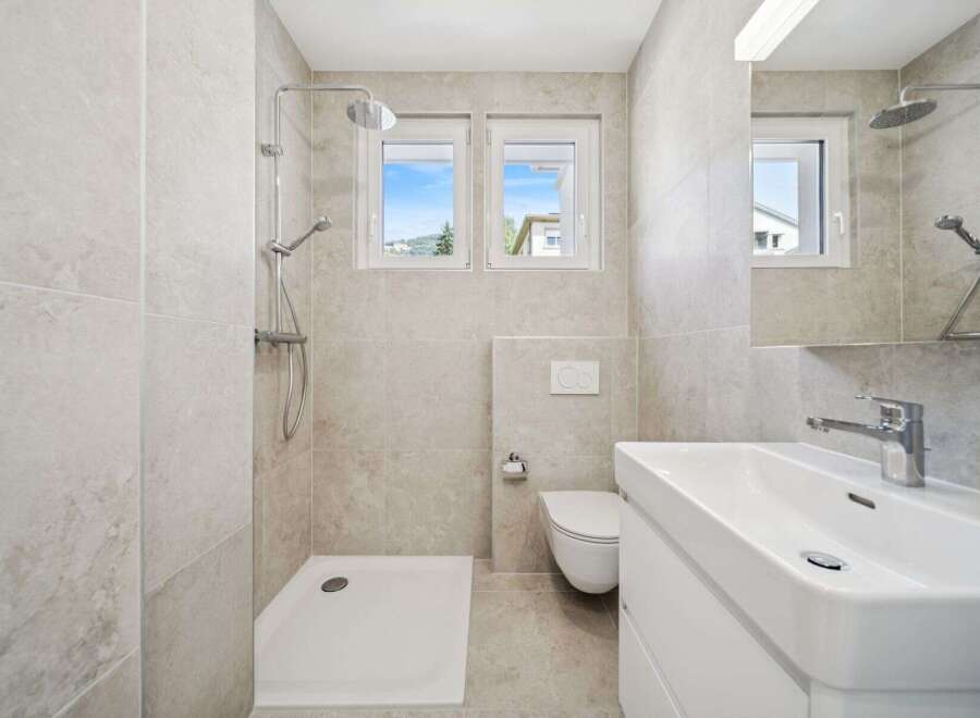 This modern bathroom features a spacious walk-in shower with a rainfall showerhead and a separate handheld shower.