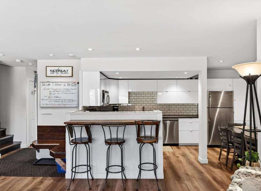 Experience a modern retreat with this stunning kitchen featuring sleek white cabinetry, a stylish subway tile backsplash, and a convenient breakfast bar with seating.