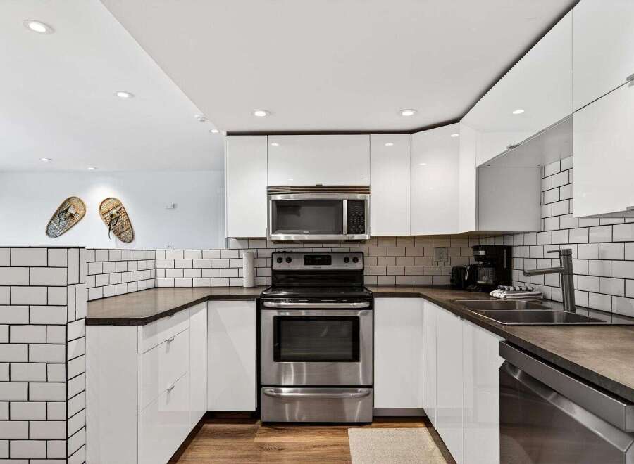 This modern kitchen features sleek white cabinetry and a stainless steel appliance suite, including a microwave and oven.