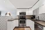 This modern kitchen features sleek white cabinetry and a stainless steel appliance suite, including a microwave and oven.