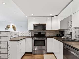 This modern kitchen features sleek white cabinetry and a stainless steel appliance suite, including a microwave and oven.