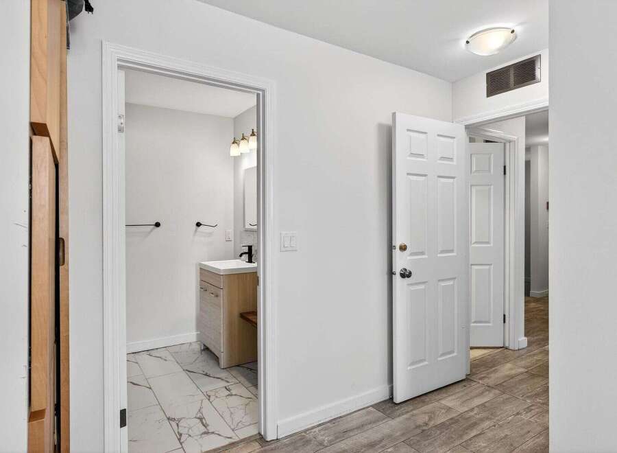 Step into a bright and airy hallway featuring a modern bathroom with a sleek vanity and marble-tiled floor.