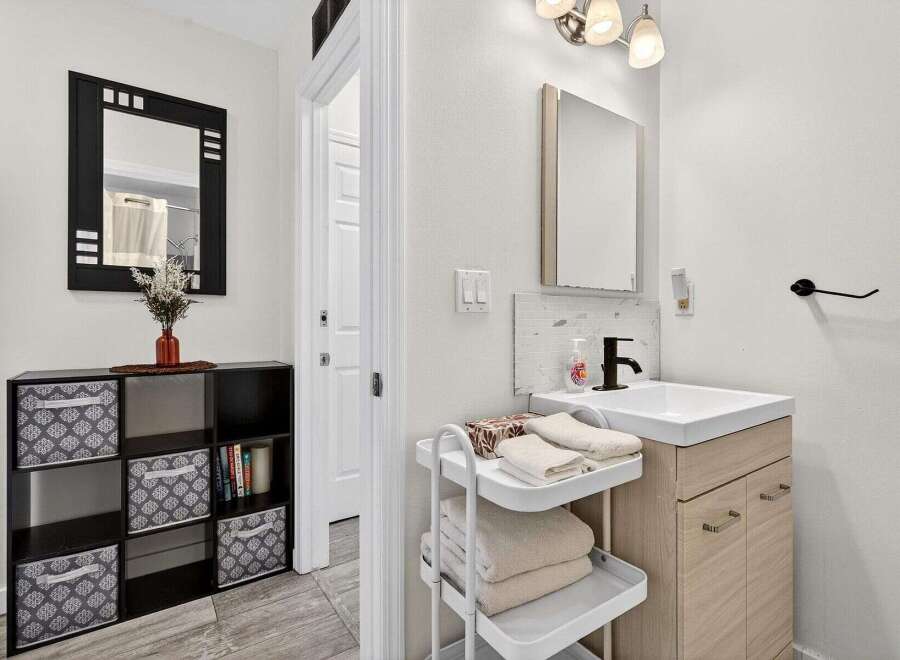 This modern bathroom features a sleek vanity with a light wood finish and a white countertop, complemented by a black faucet and a tiled backsplash.