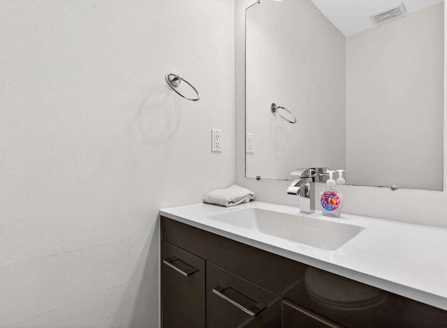 This modern bathroom features a sleek vanity with dark cabinetry and a white countertop, complemented by a minimalist sink and chrome faucet.
