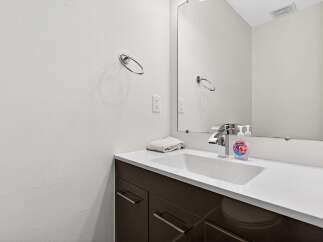 This modern bathroom features a sleek vanity with dark cabinetry and a white countertop, complemented by a minimalist sink and chrome faucet.