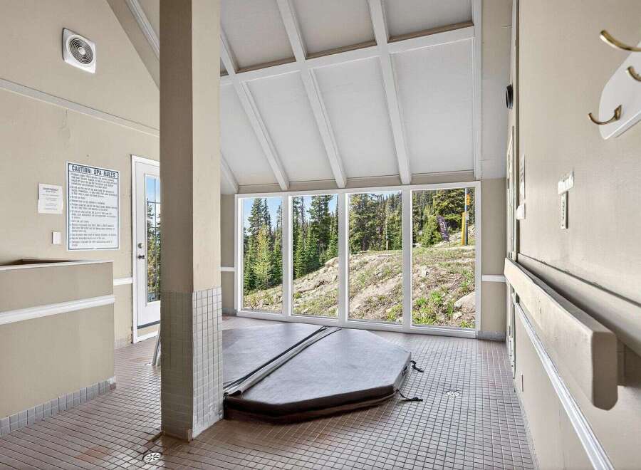 Enjoy a relaxing soak in this indoor hot tub room, featuring a large, covered spa with stunning views of the surrounding forest and ski slopes.