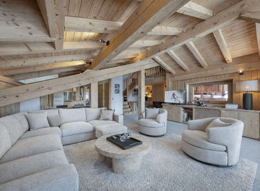 Experience luxury mountain living in this stunning chalet featuring a spacious sectional sofa and cozy armchairs perfect for relaxing by the entertainment center.