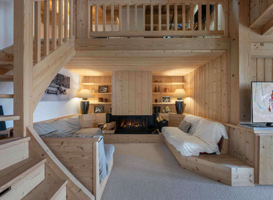 Experience cozy living in this charming wooden chalet, featuring a central fireplace and built-in seating areas perfect for relaxation.