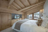 Experience rustic charm in this mountain retreat bedroom, featuring a vaulted wood-beamed ceiling and a large window offering scenic winter views.