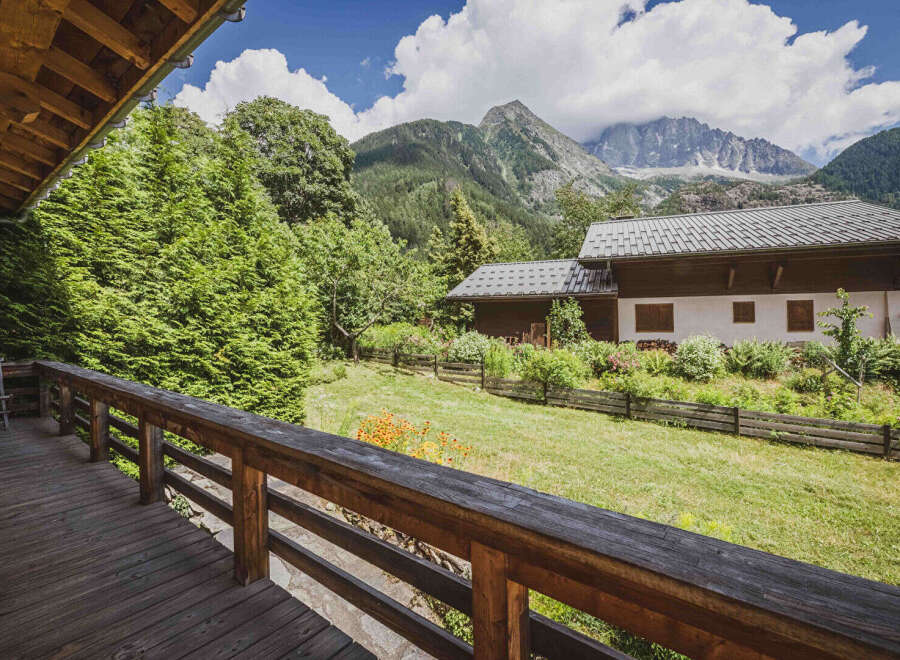 Experience the charm of mountain living with this picturesque property, featuring a cozy wooden deck overlooking a lush green lawn and a traditional alpine house.