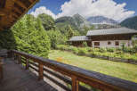 Experience the charm of mountain living with this picturesque property, featuring a cozy wooden deck overlooking a lush green lawn and a traditional alpine house.