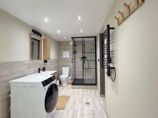 This modern bathroom features a sleek white washing machine and vanity with a black faucet, complemented by a wood-accented medicine cabinet and mirror.