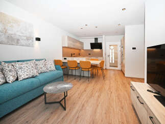 Experience modern living in this beautifully appointed apartment, featuring a comfortable teal sofa adorned with floral cushions and a sleek coffee table.