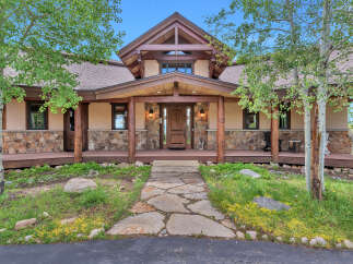 Discover this stunning mountain home featuring a grand entrance with a stone and wood facade, complemented by a spacious covered porch perfect for enjoying the serene surroundings.