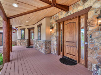 Welcome guests to this stunning mountain home with a grand covered porch featuring rustic log posts and a warm wooden ceiling.