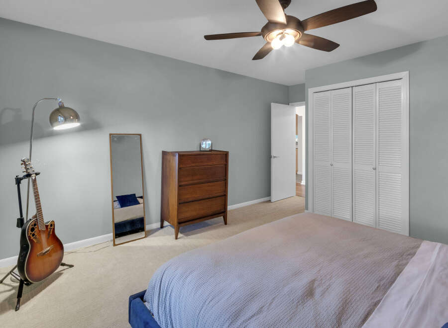 This bedroom features a comfortable bed with a textured duvet, a wooden dresser, and a full-length mirror.