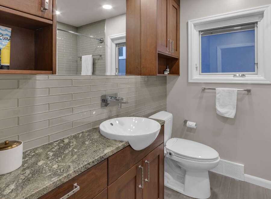 This modern bathroom features a sleek vessel sink atop a granite countertop, complemented by warm wood cabinetry.