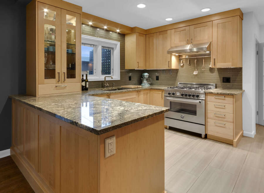 This modern kitchen boasts custom light wood cabinetry, granite countertops, and a sleek subway tile backsplash.