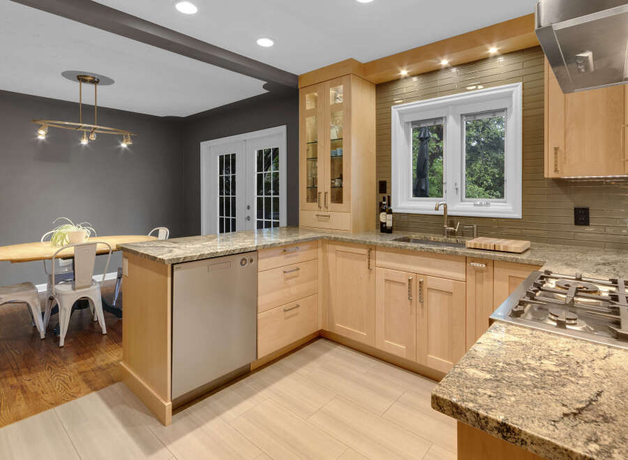 This modern kitchen boasts sleek, light wood cabinetry complemented by granite countertops and a stylish tiled backsplash.