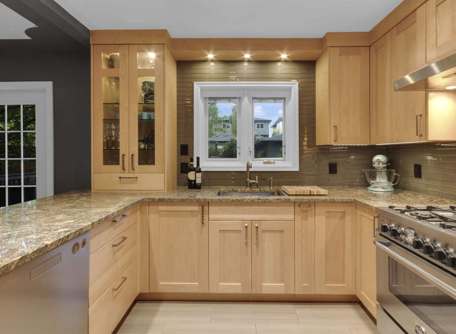 This stunning kitchen features light wood cabinetry complemented by a granite countertop and a sleek glass tile backsplash.