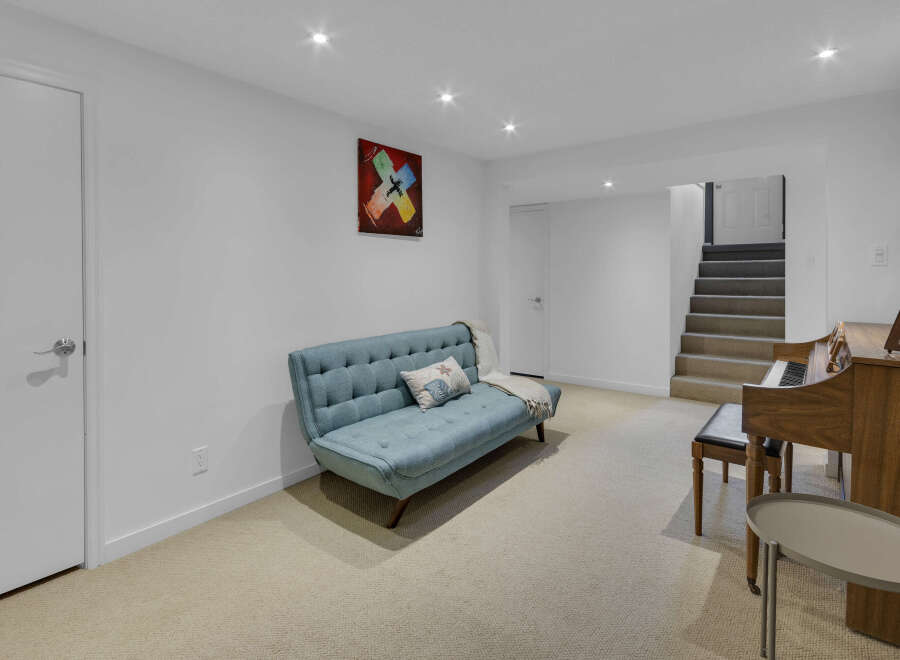 Discover comfortable living in this inviting basement space, featuring a stylish blue sofa perfect for relaxation and a beautiful wooden piano ready for musical inspiration.