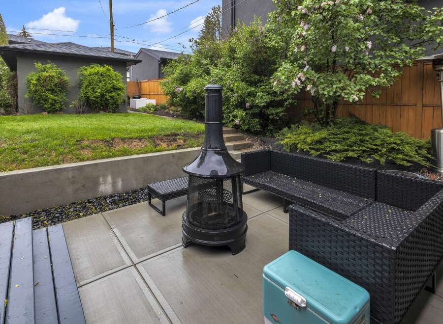 Enjoy outdoor living in this spacious backyard featuring a modern patio with a fire pit and comfortable wicker seating.