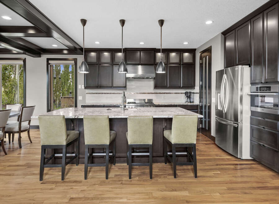 Experience luxury in this stunning kitchen featuring dark wood cabinetry, a spacious granite island with bar seating, and sleek stainless steel appliances.